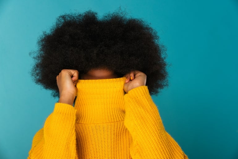 Jeune femme noire se cachant le visage avec son chandail jaune