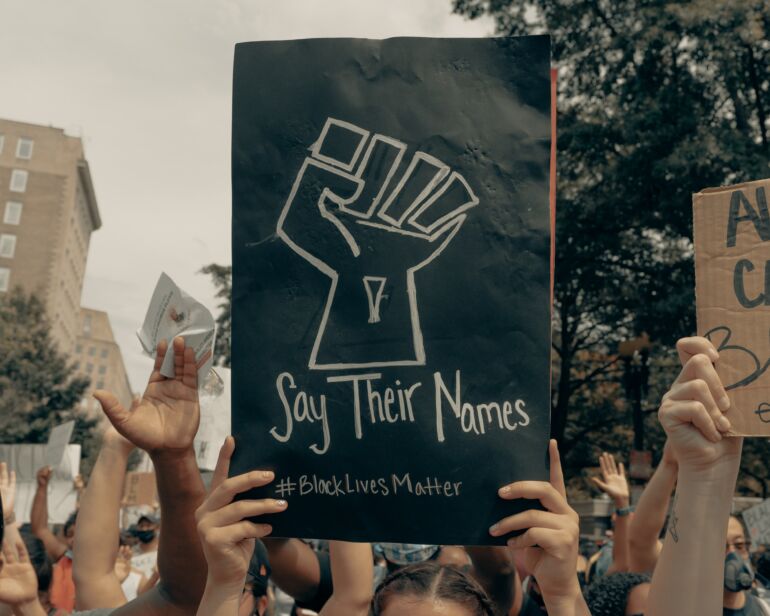 Mains tenant une affiche Say their names dans une manifestation
